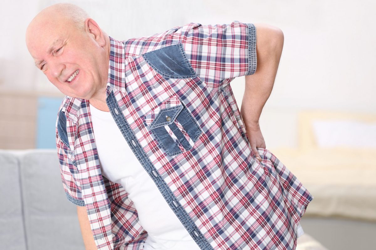 An elderly gentleman in a checkered shirt bends to the side in pain from a herniated disc.