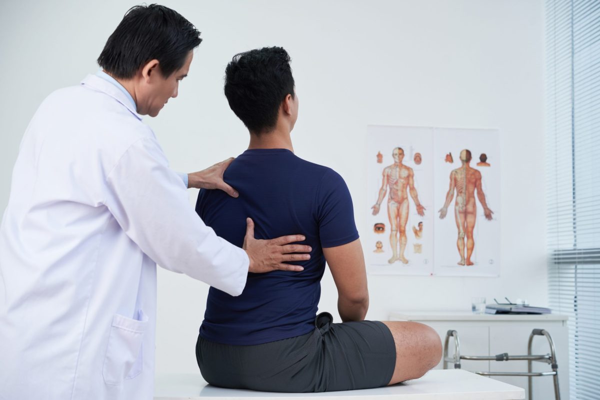  Male doctor checking spine of a young man in a medical treatment room.