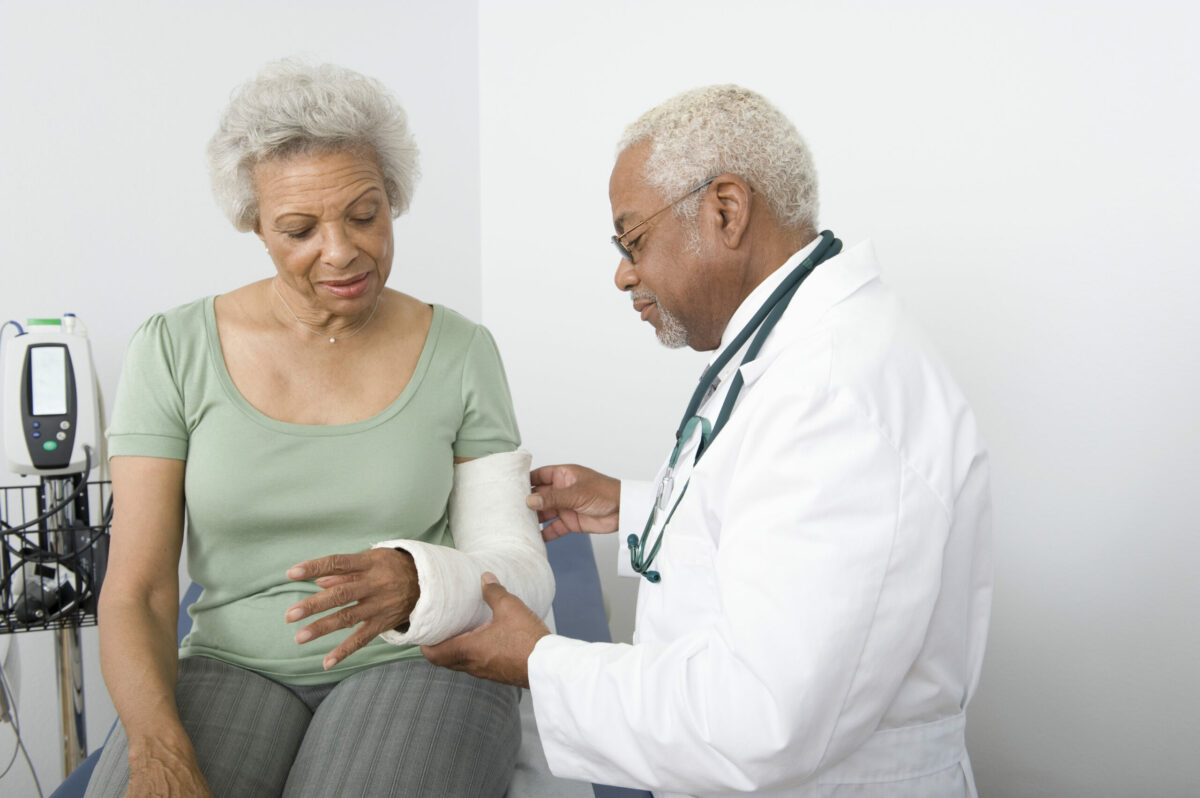 A doctor examines an older woman’s arm, which is in a cast. 
