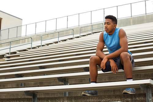 A young African American track athlete is sitting on the bleachers taking a break from running.