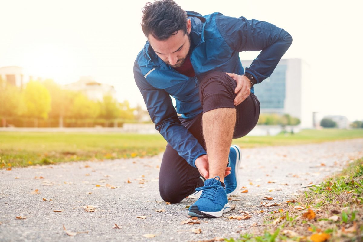  Male runner in blue jacket bending down to inspect a sprained ankle.