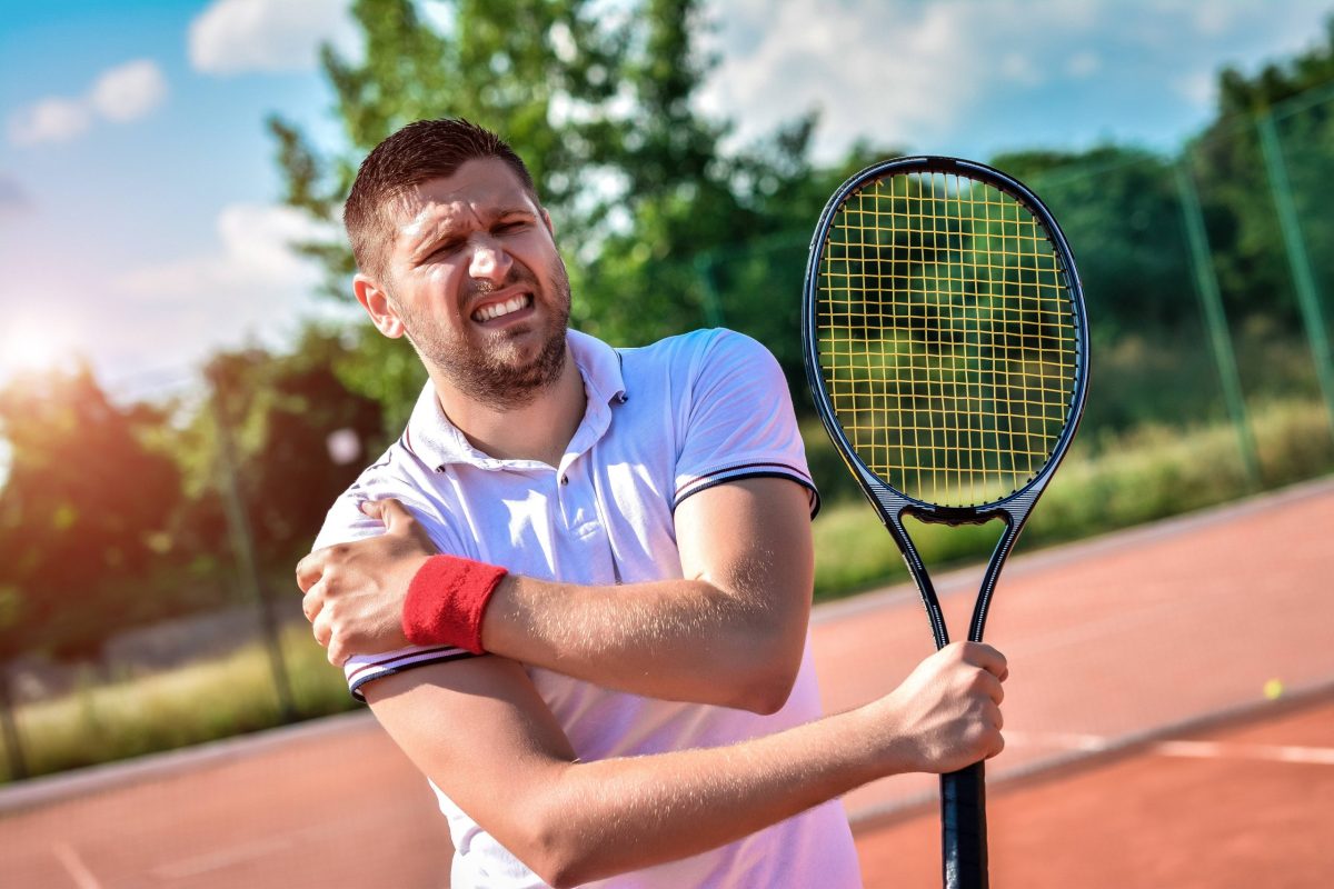 A male tennis player grasps his shoulder in pain on a tennis court indicating shoulder pain resulting from a rotator cuff tear.