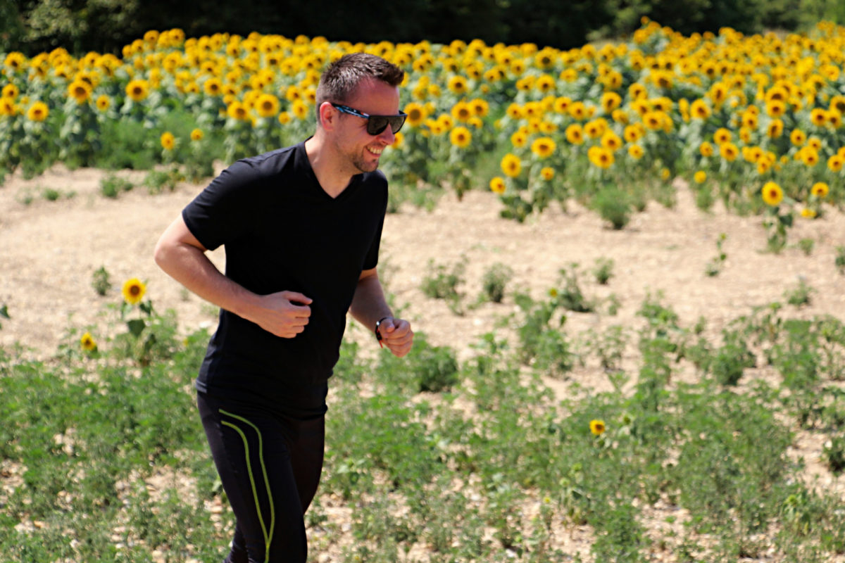 A middle-aged man is running on a trail by a field of sunflowers.