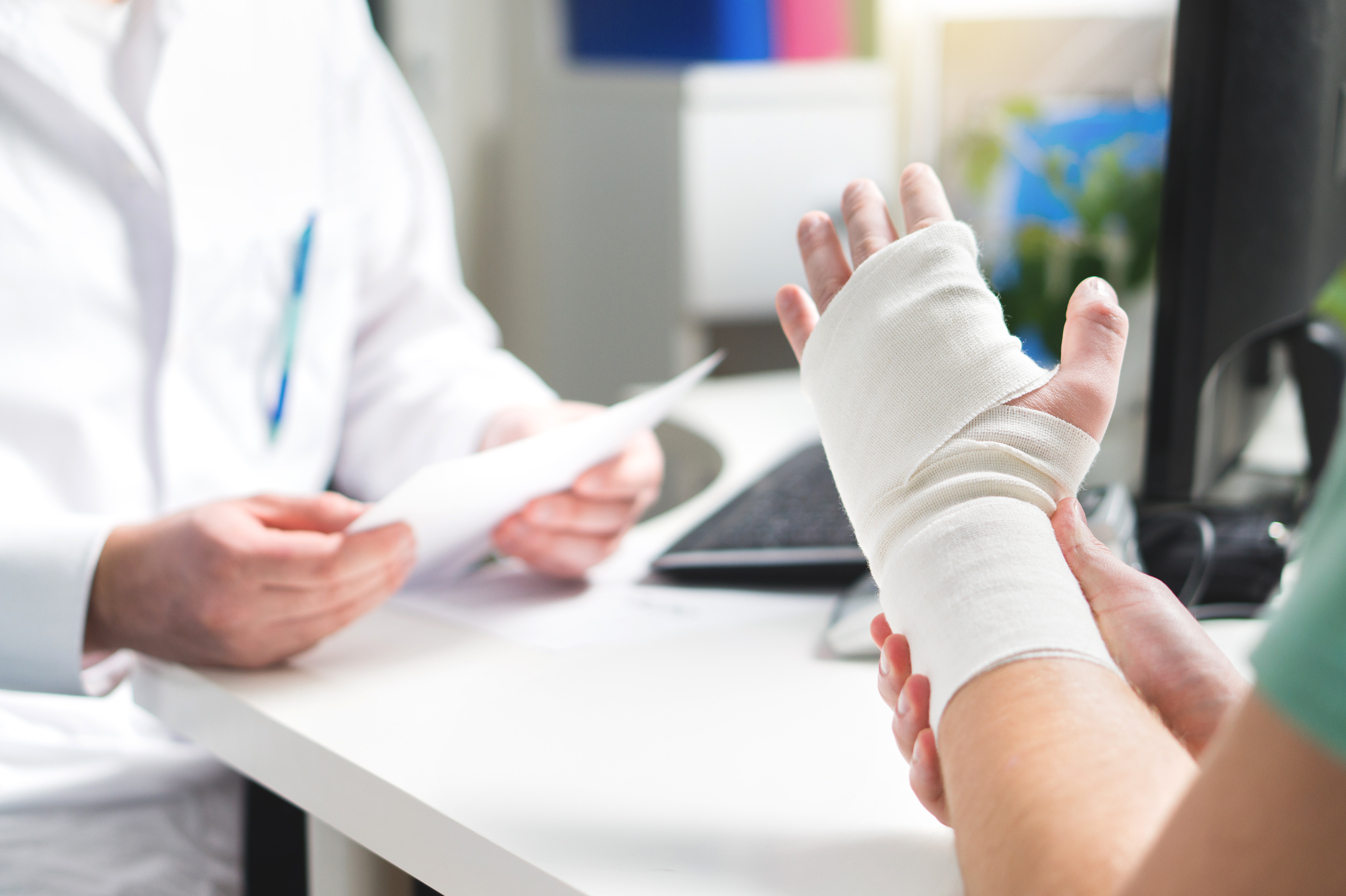 A patient with a wrapped hand and wrist injury consults with an orthopedic urgent care doctor. 