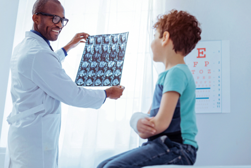 An orthopedic doctor wearing glasses examines the X-rays of a young boy with a broken arm.