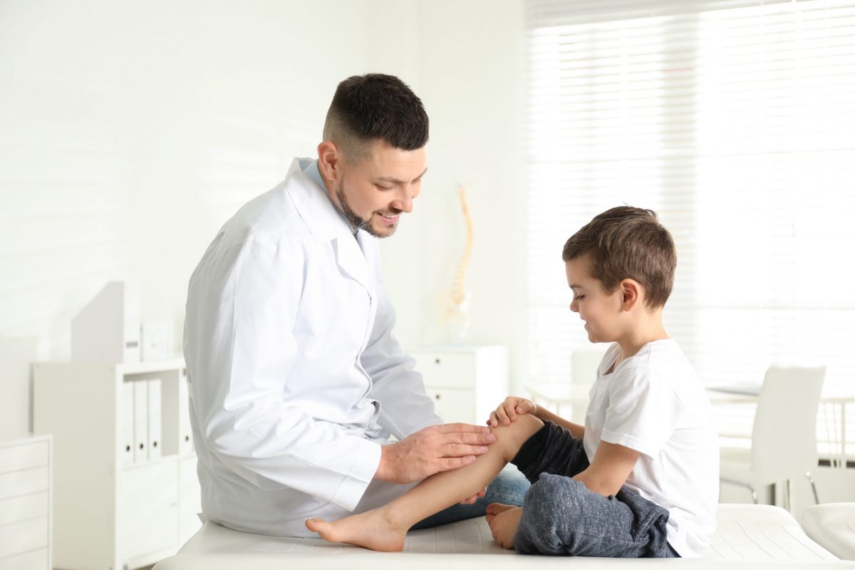 An orthopedic doctor examines a young patient’s leg in the clinic.