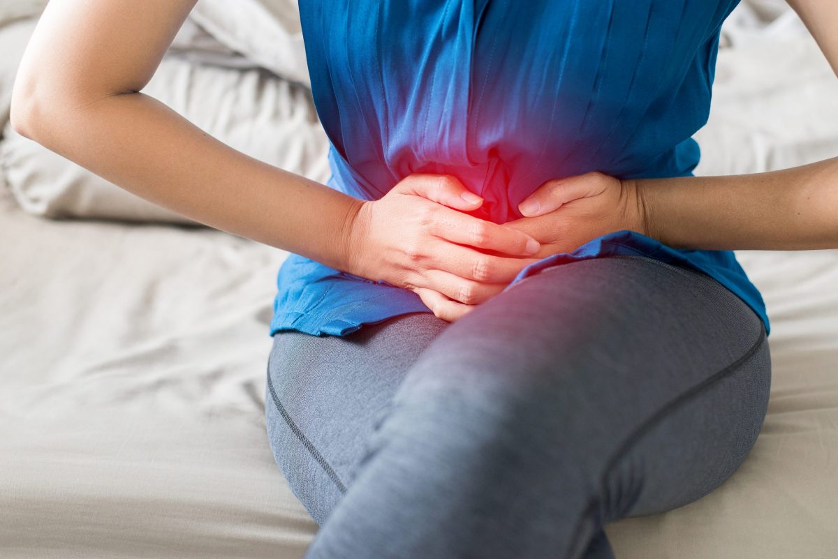 Woman in blue shirt squeezing stomach from pain, with red, glowing coloring to showcase pain. 
