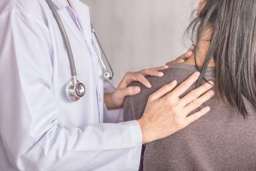 A physician in a white coat examines a female patient with neck pain.