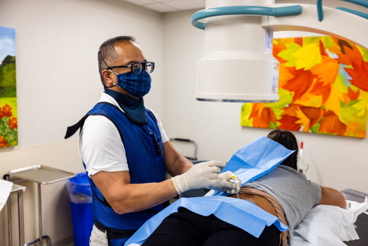 EmergeOrtho specialist with blue vest and mask working on a patient lying on her stomach.