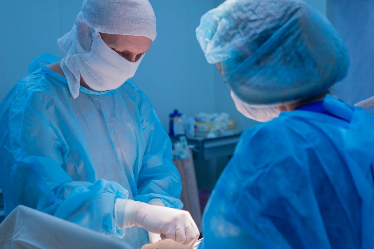 Two surgeons in PPE perform hernia surgery in the operating room.