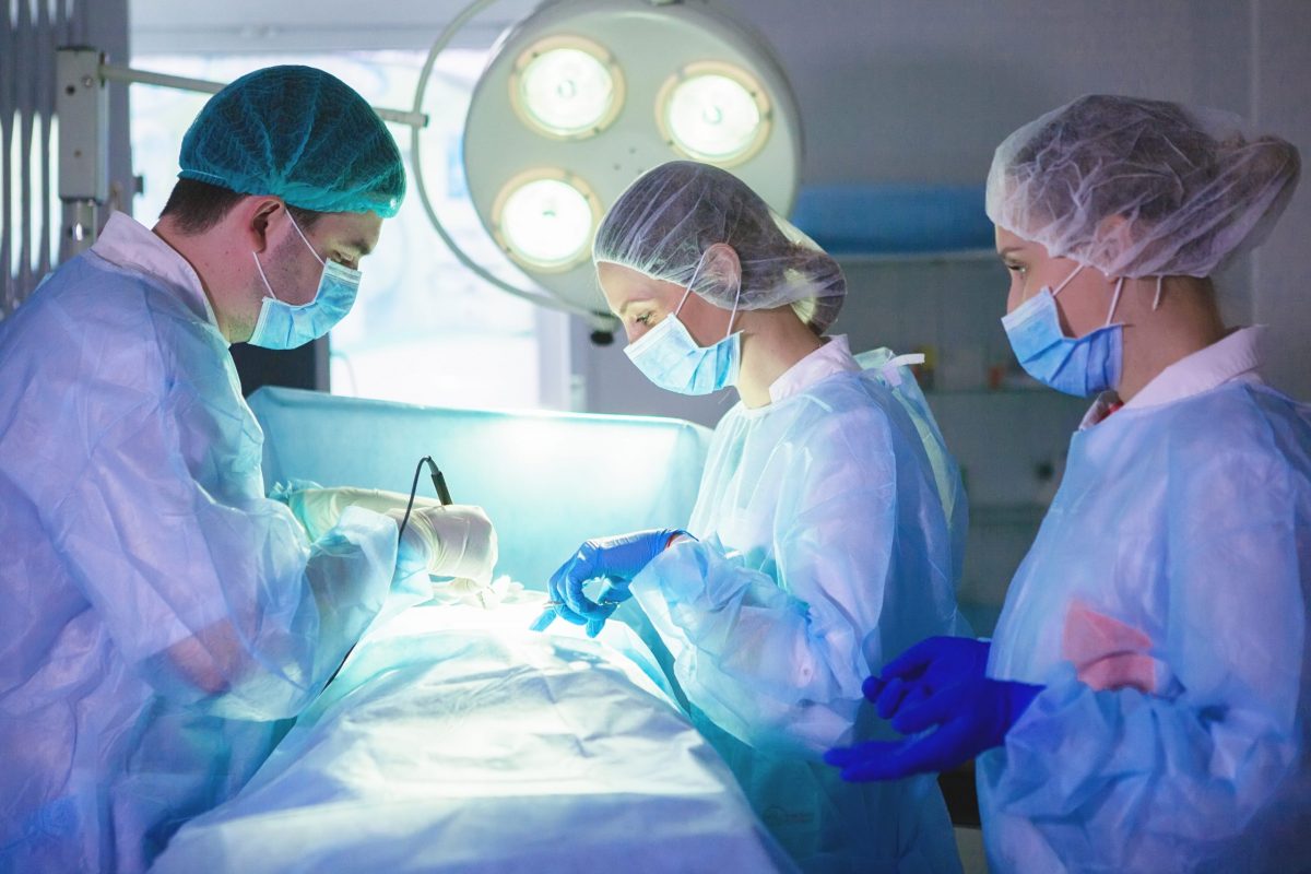 Three surgeons in PPE perform abdominal surgery in the operating room.