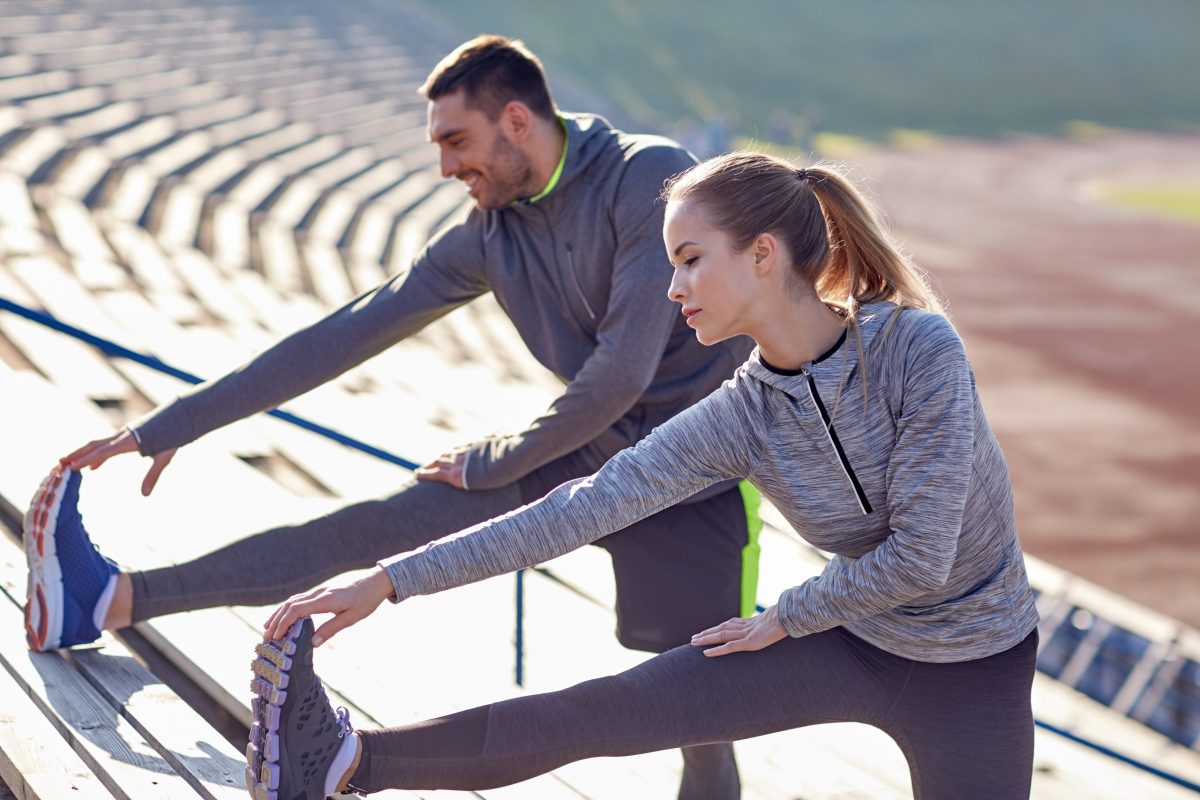 A male and female couple stretch their ankles before a run as part of their stress fracture prevention strategy on a track. 