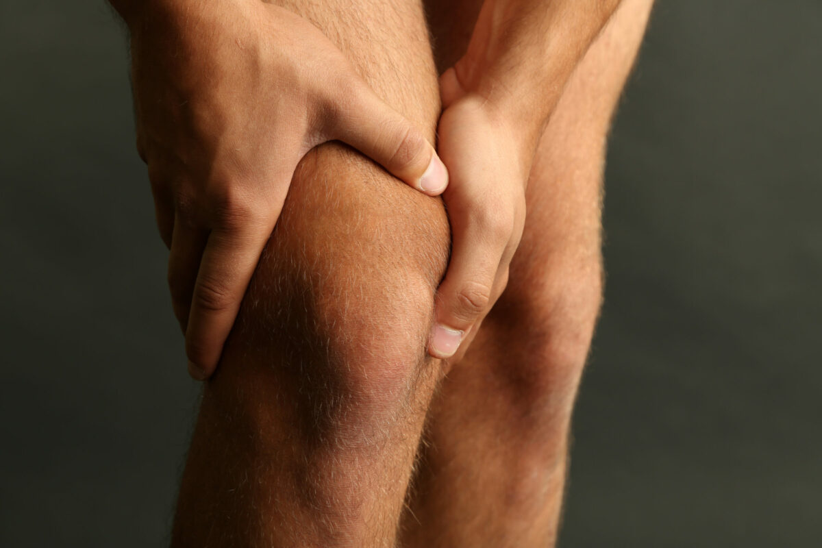 A young male crouches down to hold his quadriceps from experiencing pain above the knee cap.