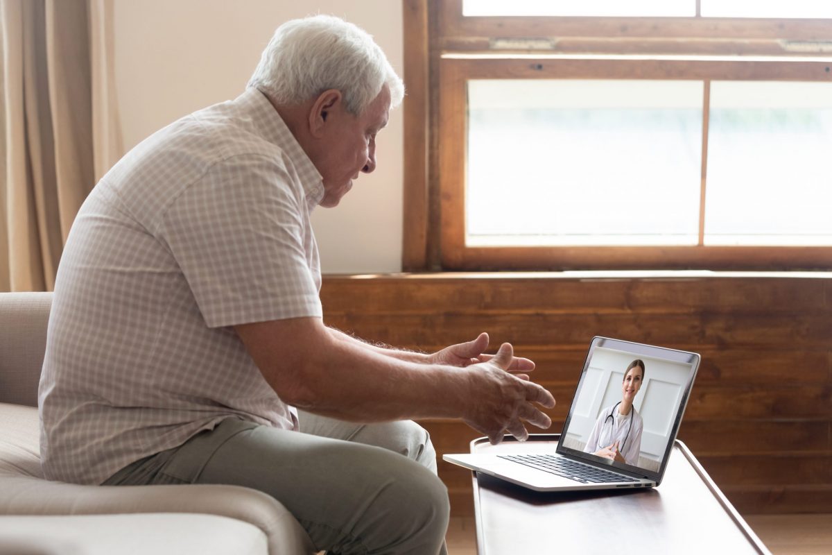 Mature man on sofa communicates with orthopedic specialist on telemedicine video call.