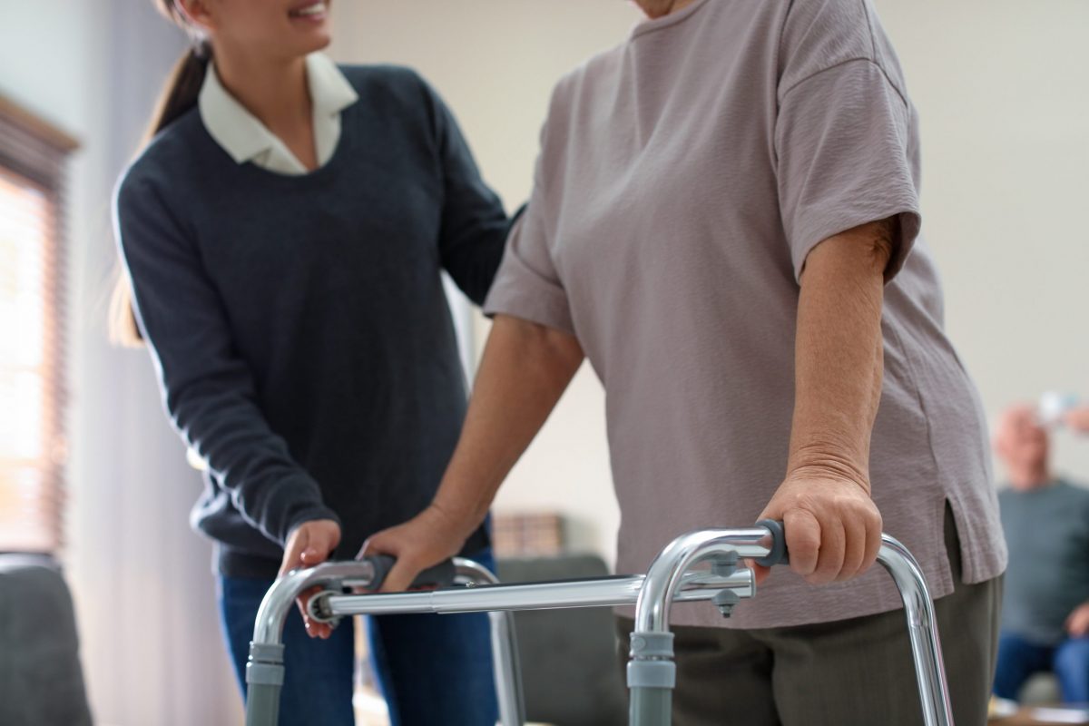 A young female physical therapist helps a mature woman use a walker after hip replacement surgery. 