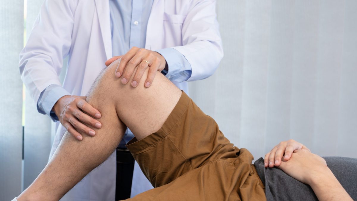 Orthopedic doctor examines a patient’s knee to determine whether he has a torn ACL.