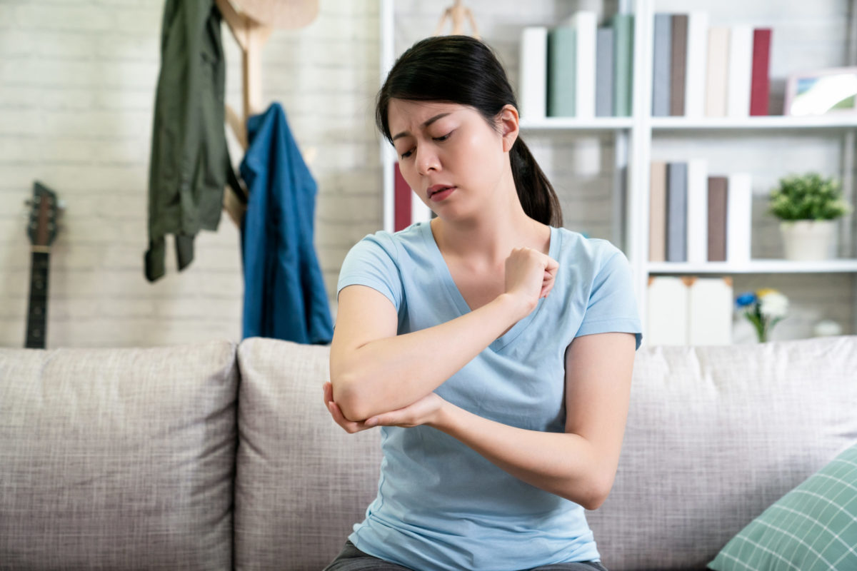 Unhappy woman massaging her elbow at home on the couch.