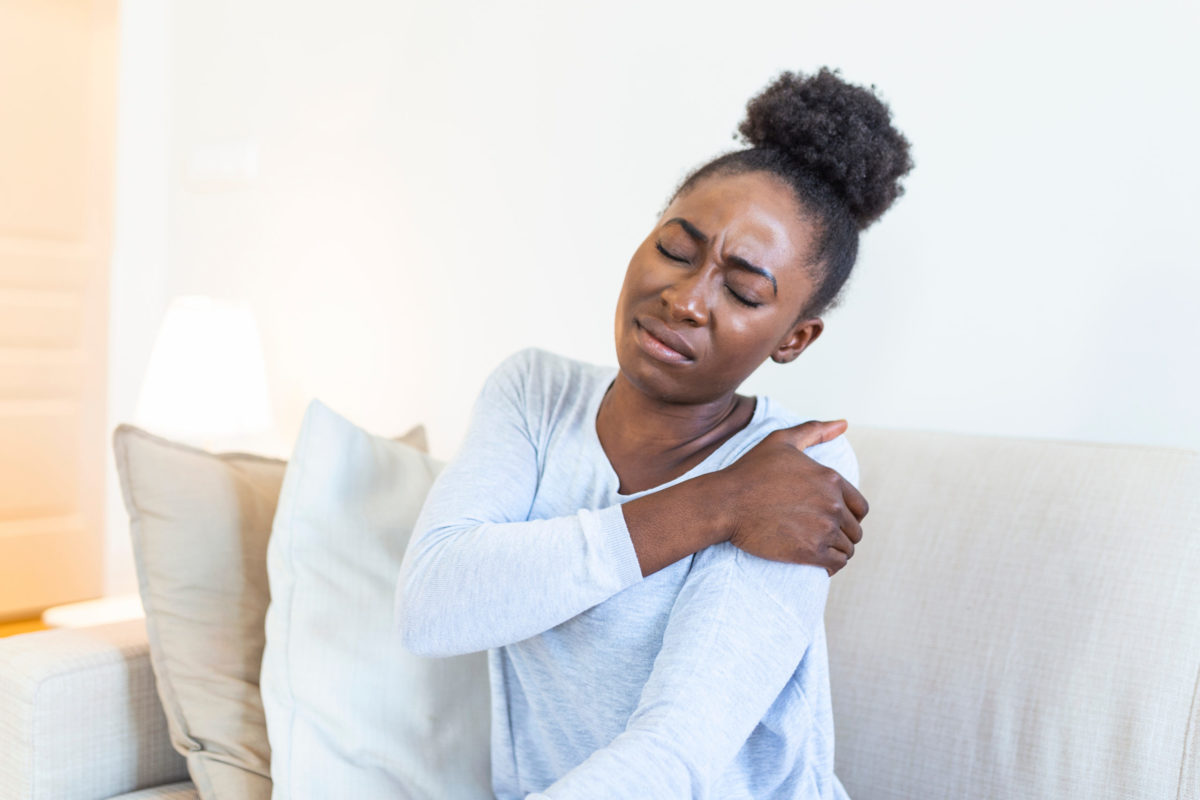 Black woman holds her shoulder in pain.