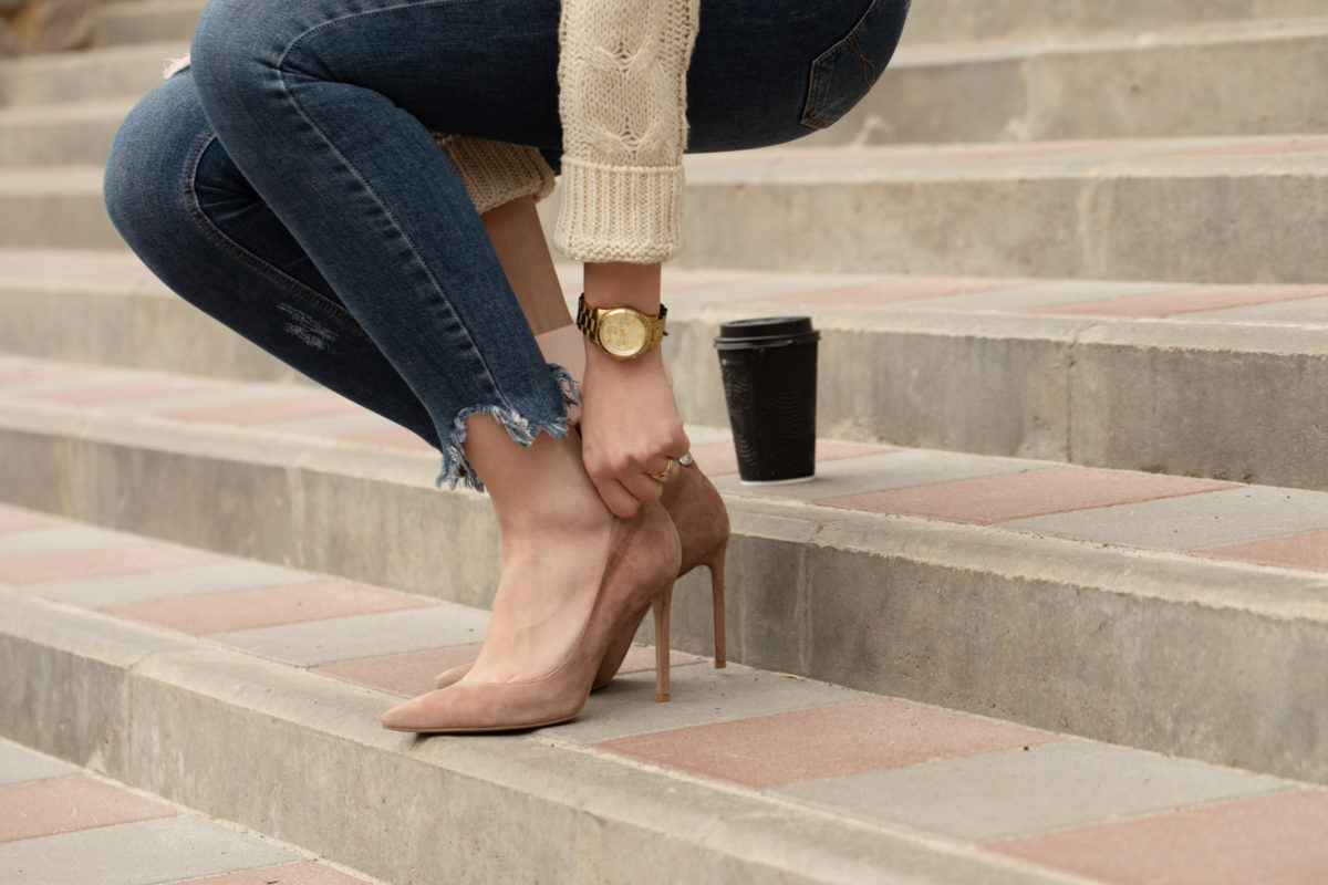  Fashionable woman adjusts her stiletto heels on a set of concrete steps. 