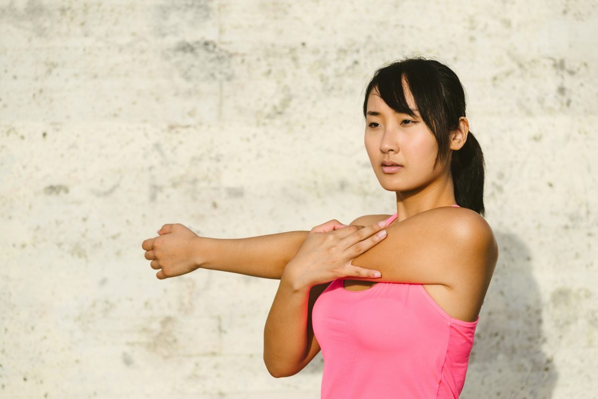 A young woman stretches her shoulder by pulling her arm across her chest.
