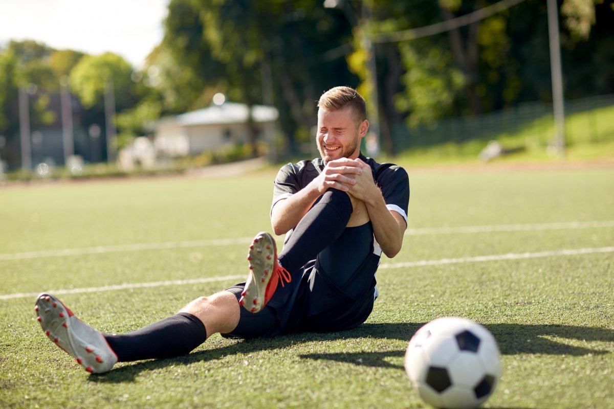 A soccer player sits on the ground holding his knee in pain. 