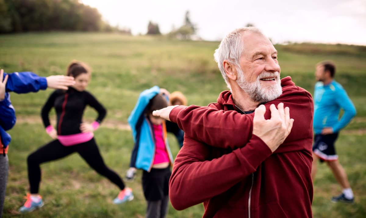  An older man stretches his shoulder before an outdoor workout.