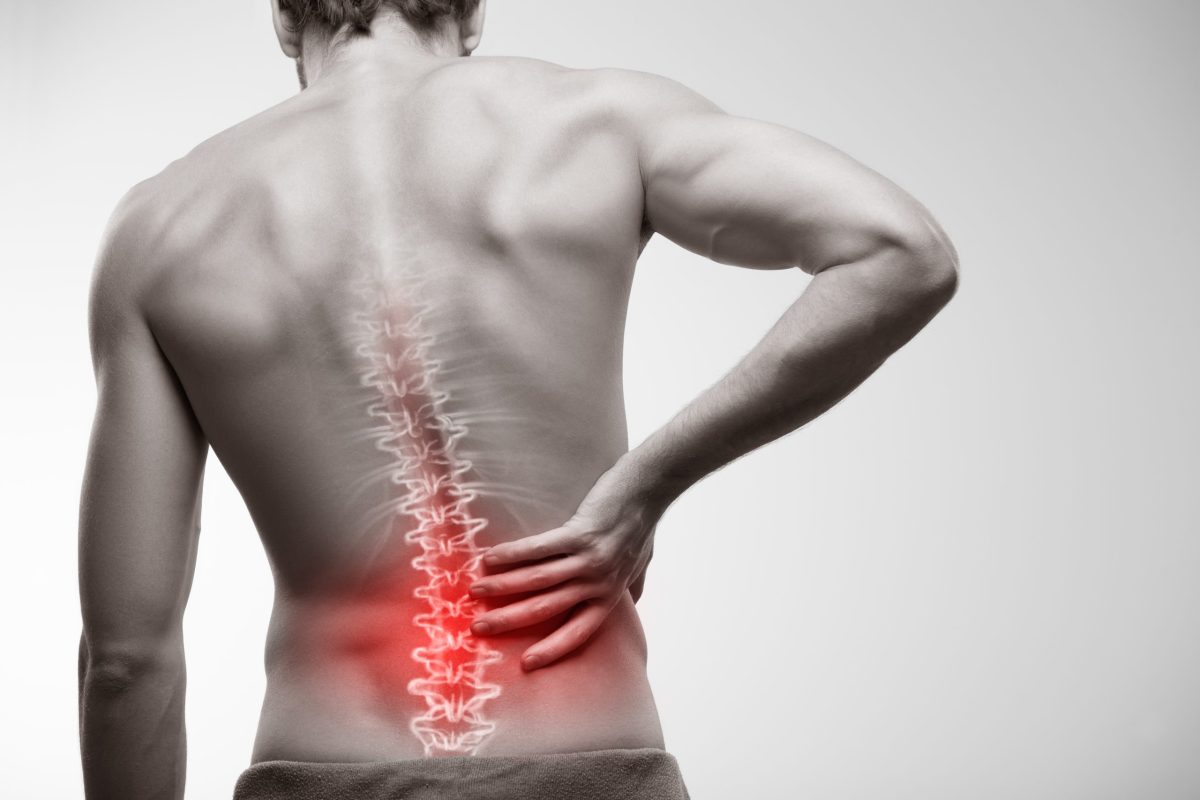 Image of male holding his back right with a x-ray image of a spine superimposed and highlighted in red.