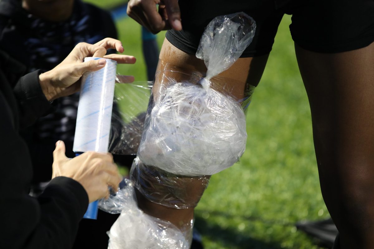  An athletic trainer wraps plastic-wrap around an ice bag to help the knee/leg injury of a female student-athlete after a game. 