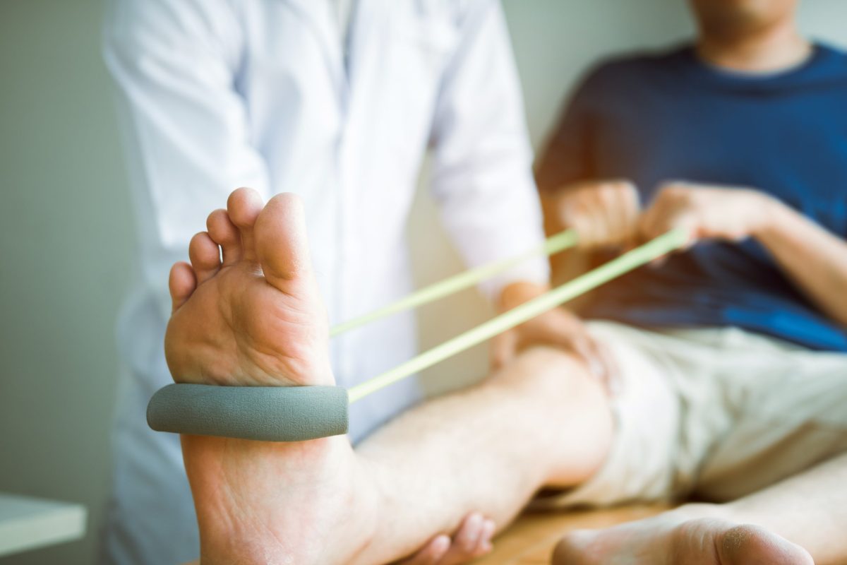 A foot and ankle doctor helps a male patient practice post foot and ankle surgery stretches with an elastic band.