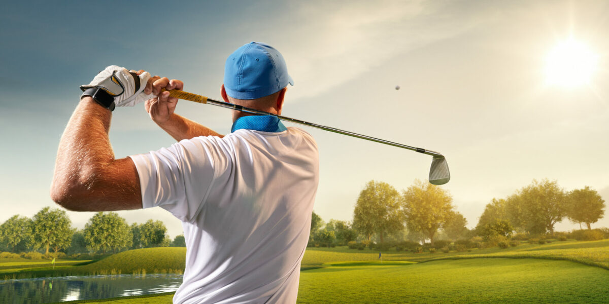 Male golfer swinging golf club on golf course. 