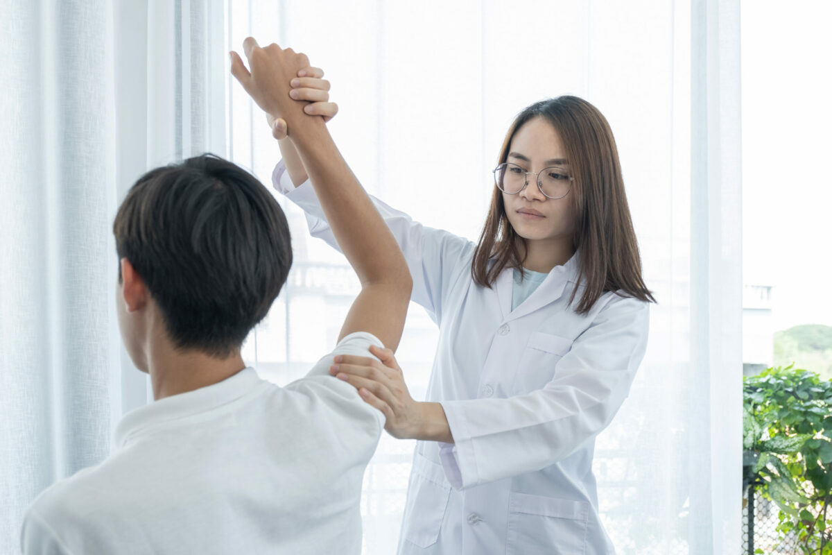 A female doctor helping a young male patient with a shoulder exercise. 
