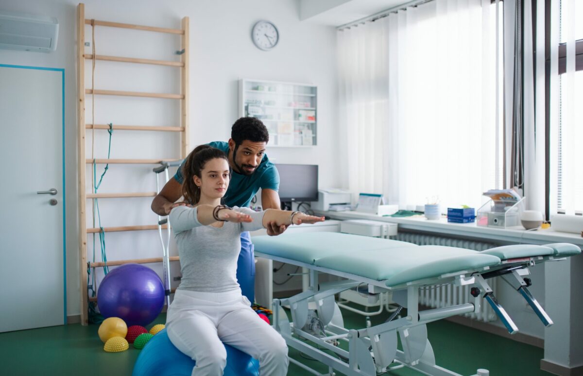  Male physical therapist doing shoulder exercises with a woman in a doctor’s office.

