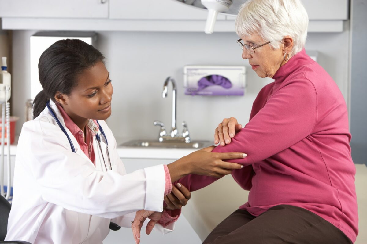 An orthopedic doctor examines a senior female patient’s left elbow in a medical facility.