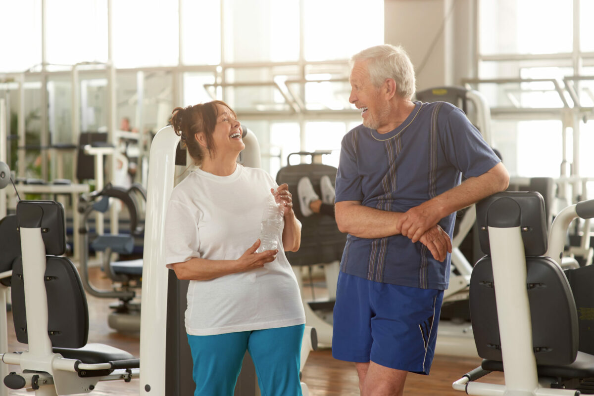 A man and woman laugh together at a gym.
