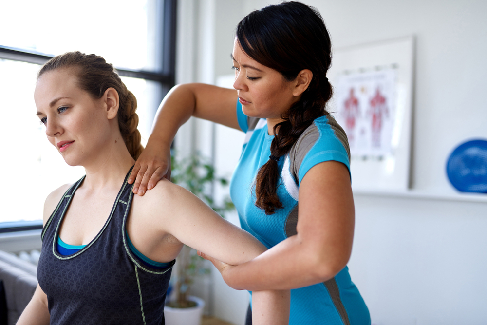 A young female physical therapist evaluates a patient’s arm and shoulder. 