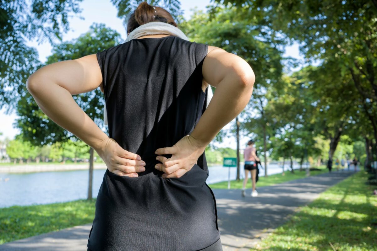 A woman walks outside with her hands on her lower back.
