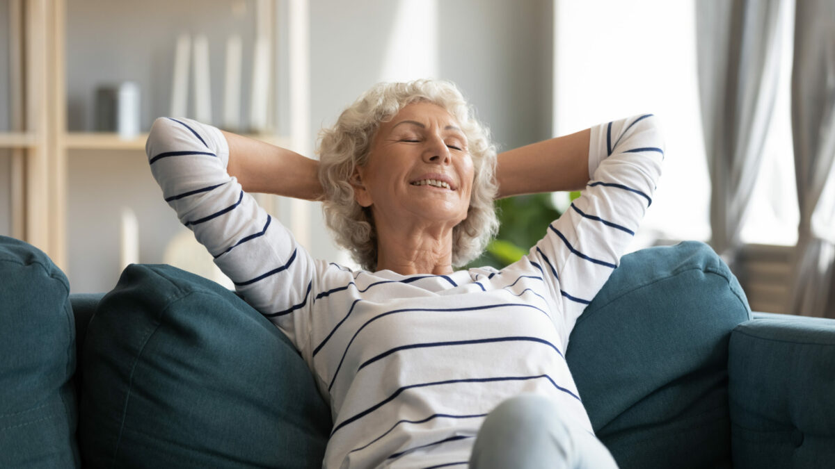 A senior female leaning back on a couch smiling and relaxed. 
