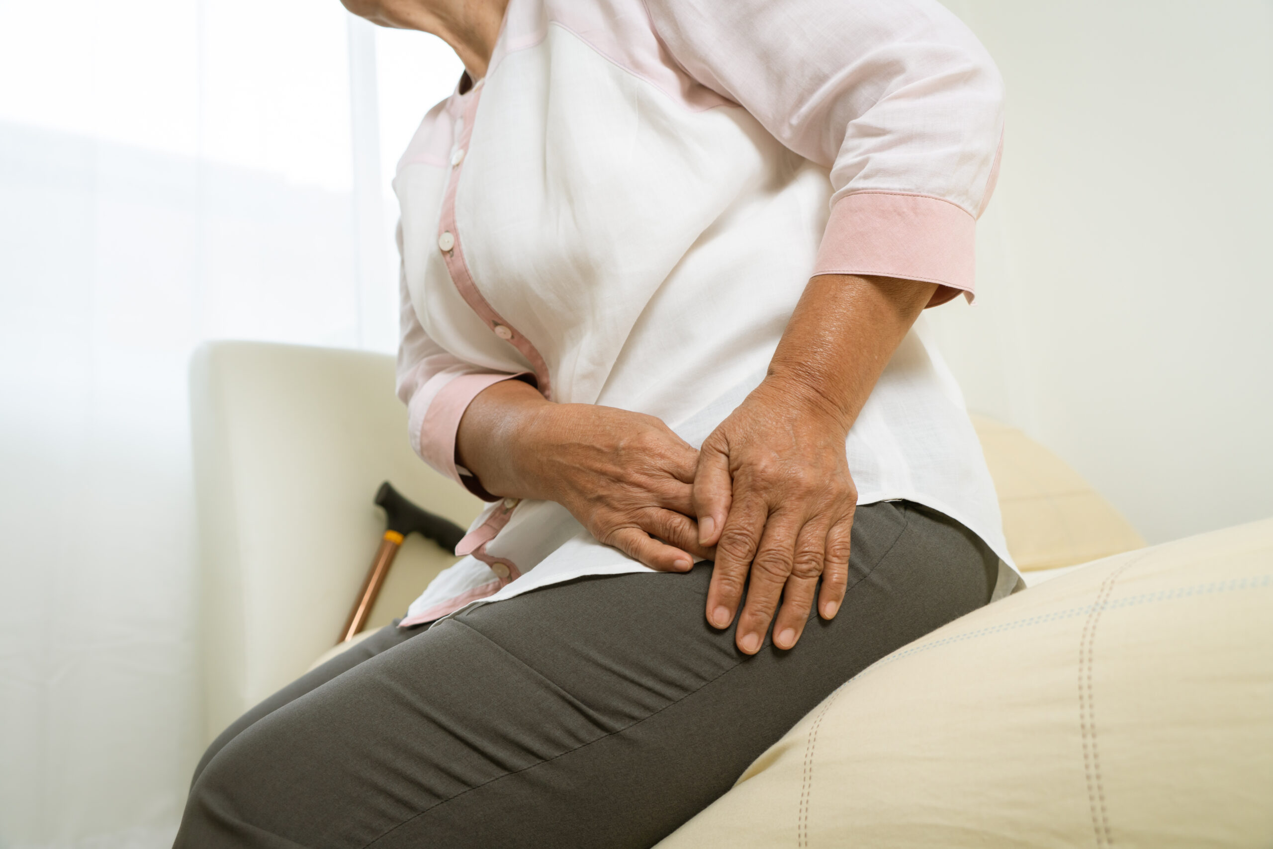 A senior woman sitting and holding her hip with two hands in pain. 