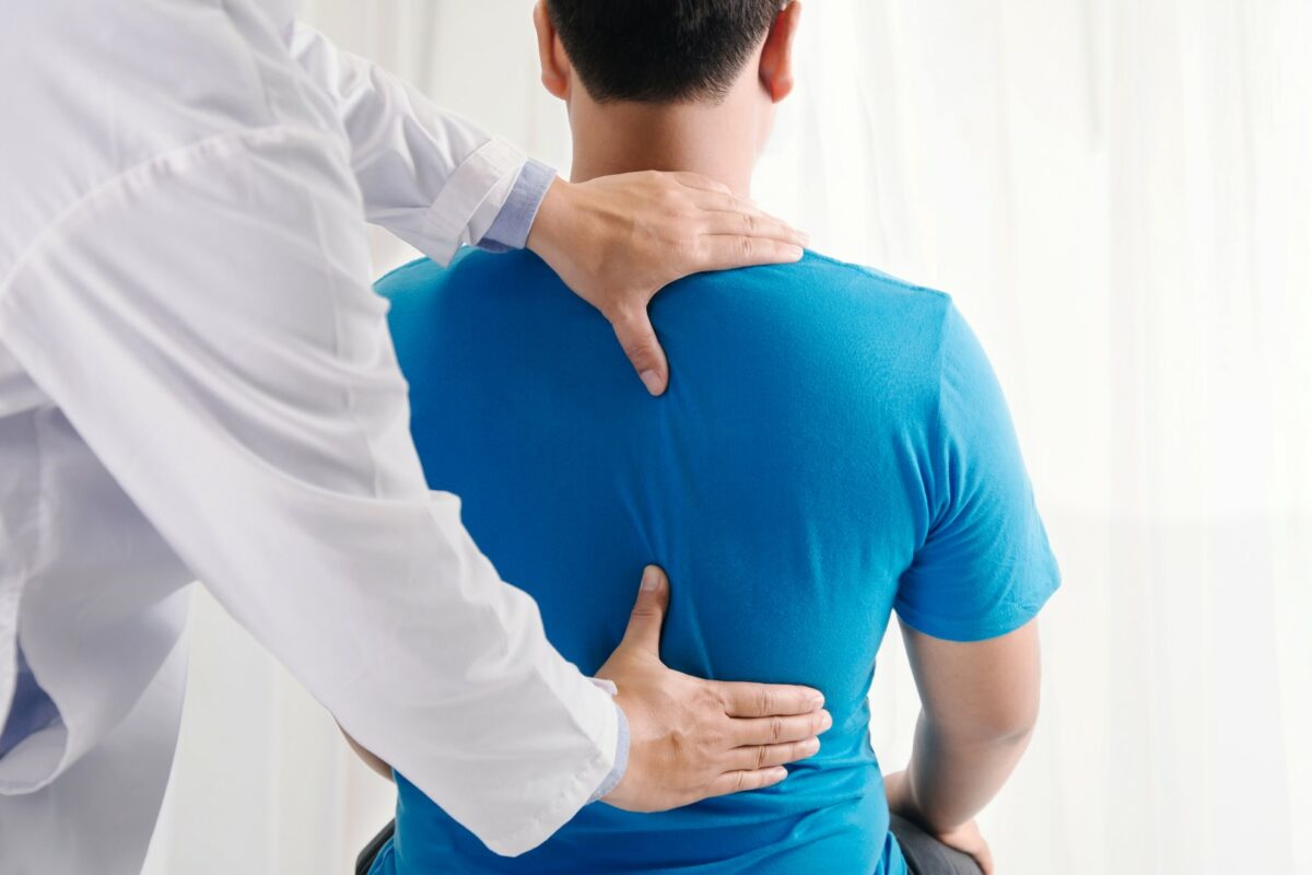 A back pain doctor examines a patient in a blue shirt. 