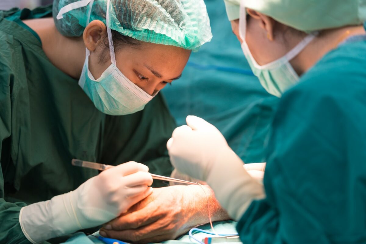 A surgeon wearing personal protective equipment (PPE) is performing surgery at an orthopedic surgery center. 