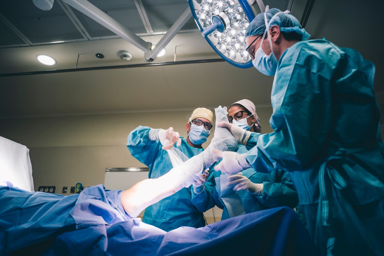 A surgical team wearing blue personal protective equipment (PPE) performs knee surgery at an orthopedic surgery hospital.